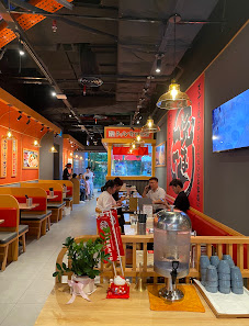 The image shows an interior view of a restaurant with modern decor featuring red and orange tones on the walls. There are several tables occupied by d