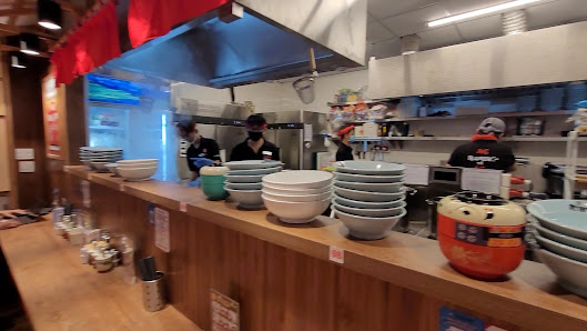 The image depicts the interior of a commercial kitchen in Thao Dien, Saigon. It features a wooden counter with stacked bowls, plates, and a red pot. S