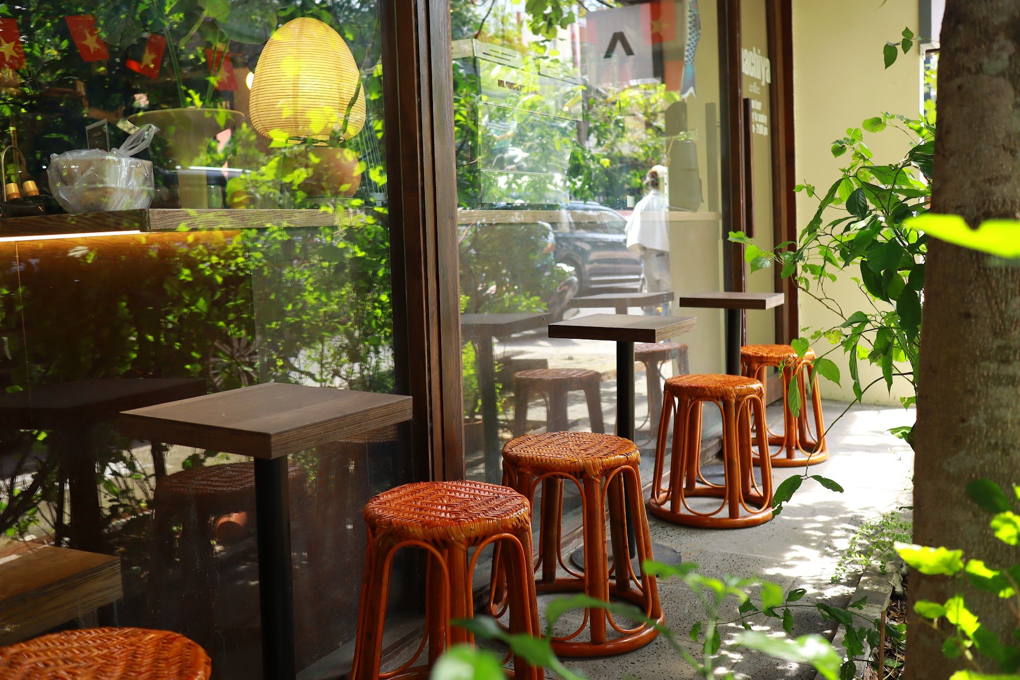 The image depicts an interior view of a cafe or restaurant in Thao Dien, Saigon. The focus is on the seating area with several woven rattan stools pla