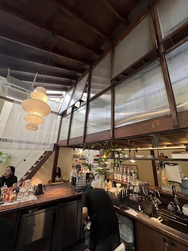 The image depicts an interior view of a modern café or restaurant with wooden beams on the ceiling and large glass windows allowing natural light to f