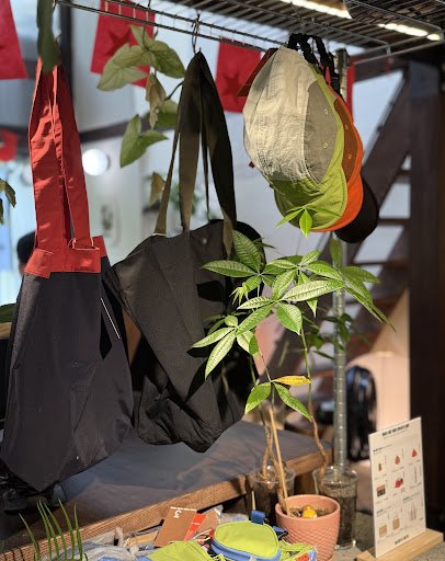 The image shows a collection of bags and hats hanging from the ceiling in an indoor setting with various items displayed on shelves below, including p