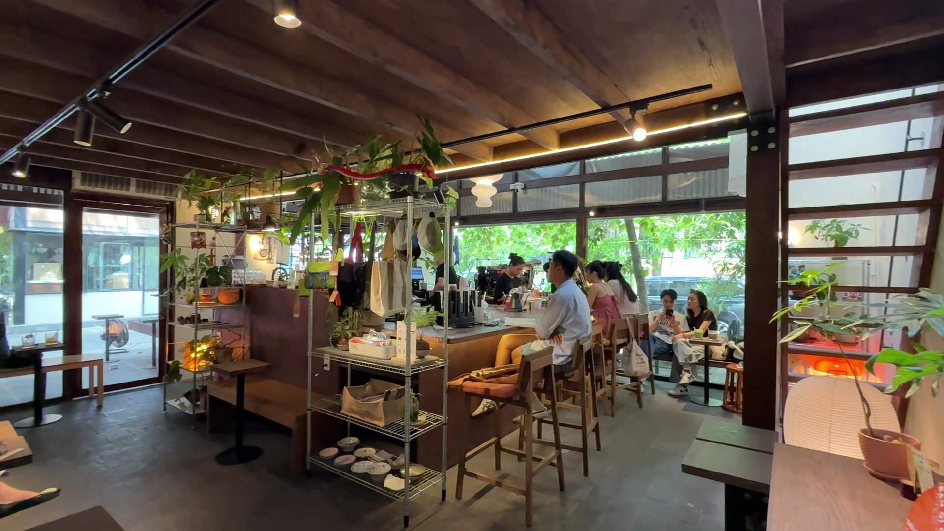 The image shows an interior view of a cozy café or restaurant in Thao Dien, Saigon. The space is warmly lit with natural light coming through large wi