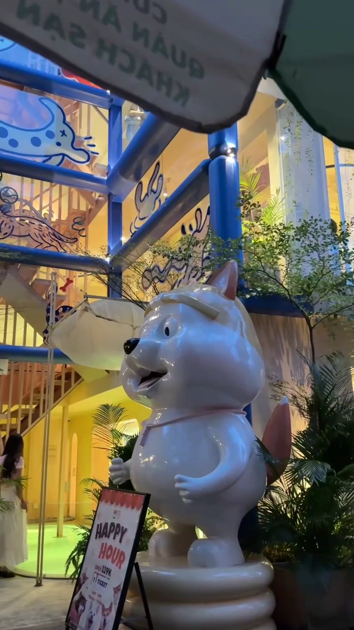 The image depicts the interior of a vibrant venue in Thao Dien, Saigon. A large white cartoon dog statue (resembling a character like Doraemon) stands