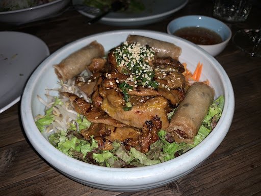A plated dish consisting of a stir-fried meat and vegetable mixture topped with sesame seeds, served over lettuce leaves alongside spring rolls on the