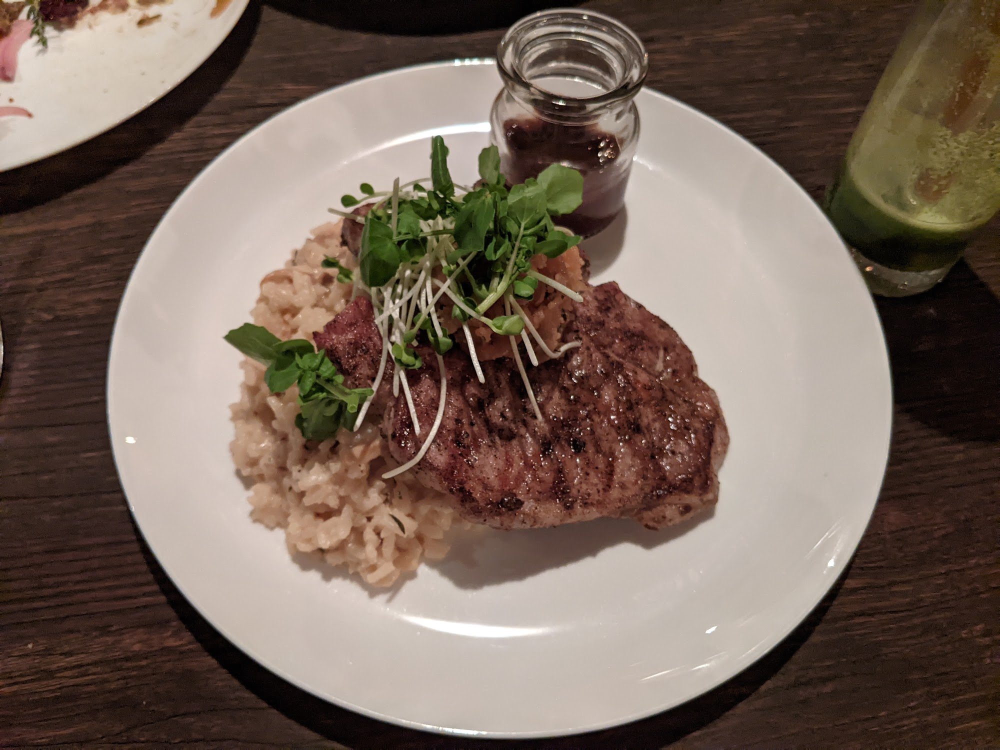 A plated dish featuring a grilled steak topped with microgreens and served alongside rice pilaf.