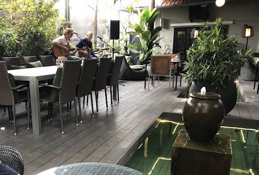 The image depicts an outdoor seating area of a restaurant or café in Thao Dien, Saigon. Two individuals are seated at opposite ends of the table playi