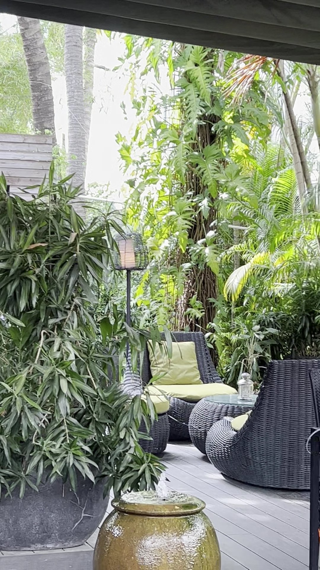 The image depicts an outdoor seating area of a venue in Thao Dien, Saigon. It features comfortable wicker chairs with green cushions and is surrounded