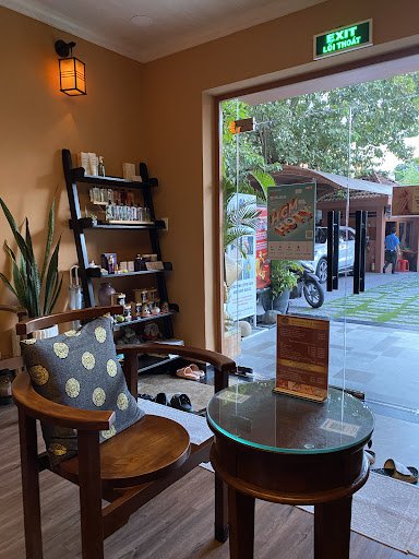 The image shows an interior view of a cafe or restaurant in Thao Dien, Saigon. A wooden chair with a patterned cushion is placed near a round glass-to