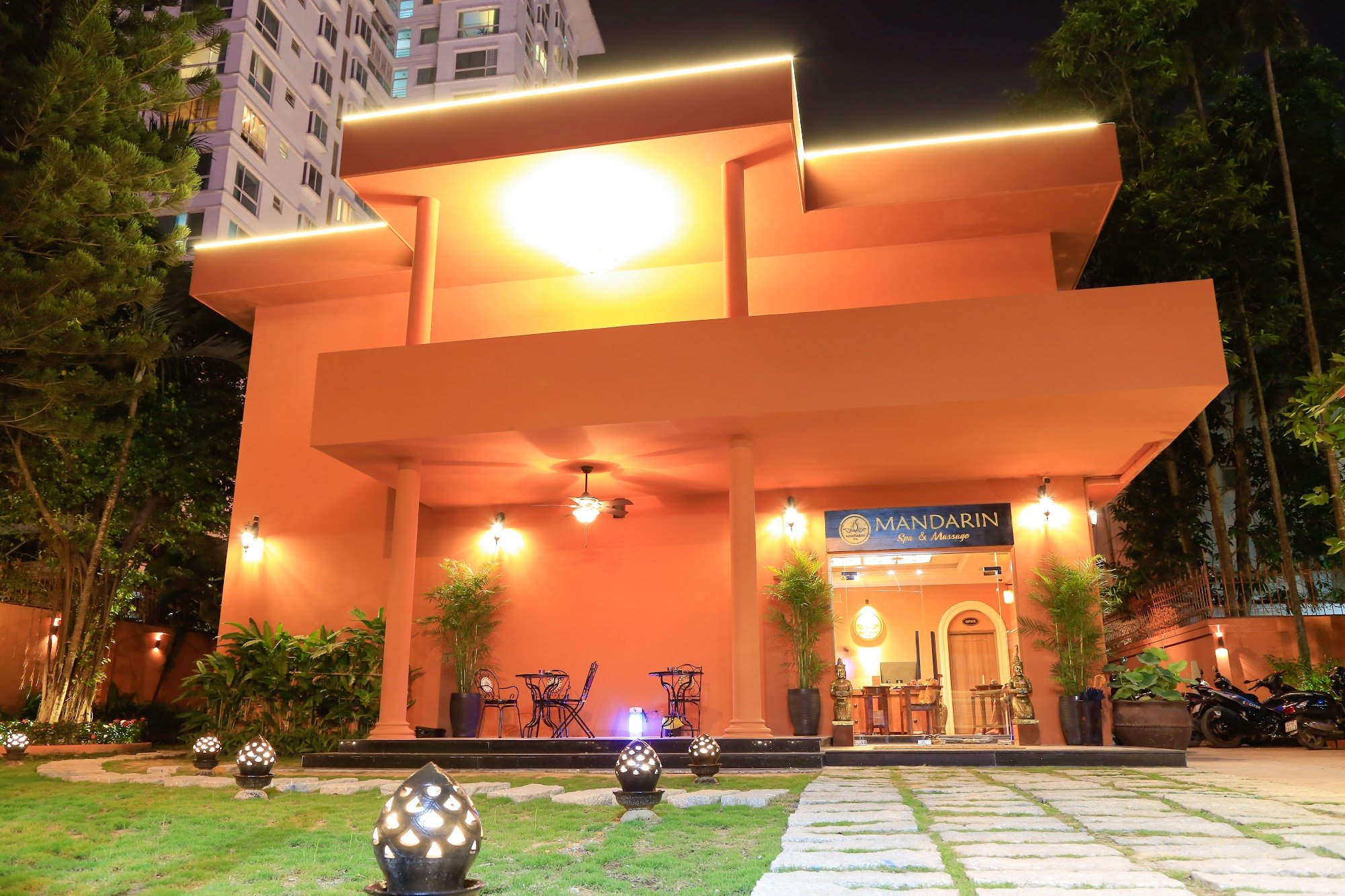 Exterior night view of Mandarin Spa & Massage in Thao Dien, Saigon. Features a modern orange building with layered architectural design, illuminated b