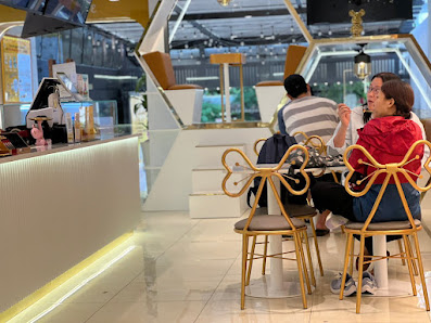 The image depicts the interior of a modern café or restaurant in Thao Dien, Saigon. Two people are seated at a table with golden chairs and a white ta