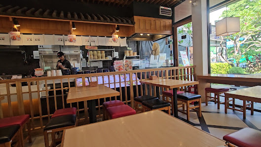 The image depicts the interior of a restaurant in Thao Dien, Saigon. It features wooden tables and chairs with red and black cushions, a counter area
