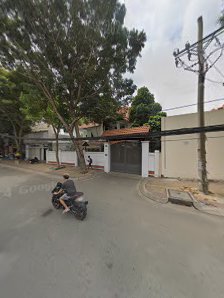 A street view showing a motorbike rider on the road in front of residential buildings with trees and power lines visible.