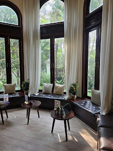 The image shows a well-lit interior space featuring large windows draped in white curtains that allow natural light to fill the room. There are severa