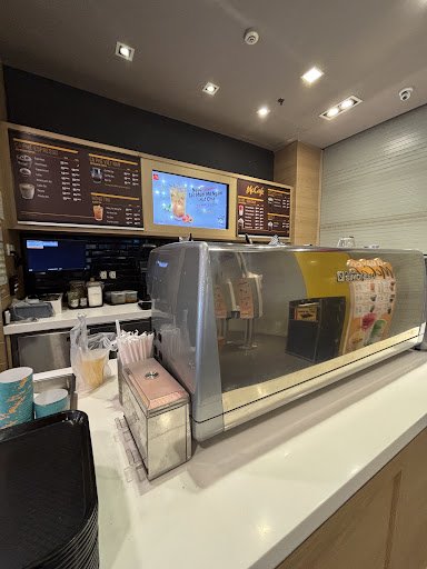 The image shows an interior view of a McDonald's restaurant counter area featuring various menu boards with food and drink options displayed, along wi