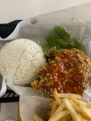 The image shows a meal consisting of fried chicken with sauce on top, served alongside French fries and a side of white rice. There is also a portion 