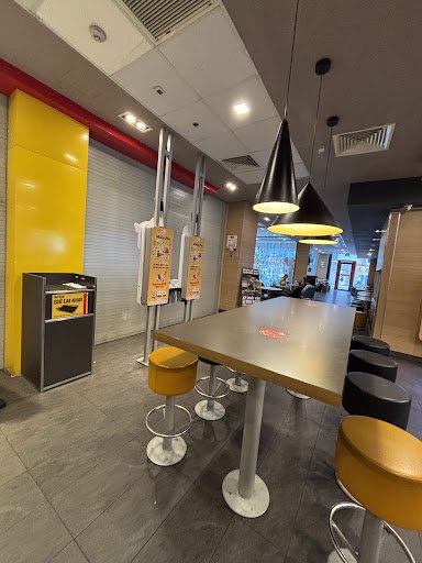 The image shows an interior view of a modern fast-food restaurant featuring yellow and metallic accents on the furniture and decor.