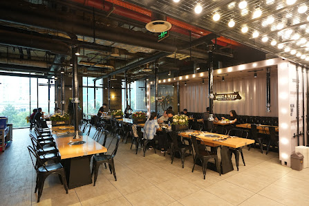 A modern industrial-style restaurant interior in Thao Dien, Saigon, featuring exposed ceiling pipes, hanging string lights, large windows with natural