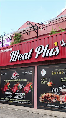 The image depicts the exterior of 'Meat Plus,' a restaurant located in Thao Dien, Saigon. The building features a red metal facade with the restaurant