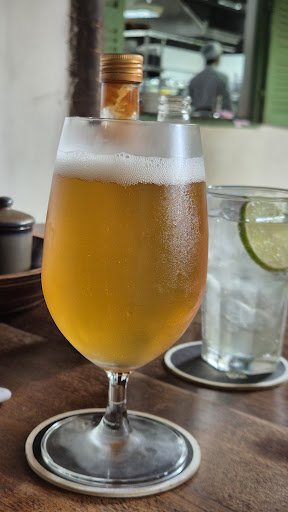 A glass of beer topped with a slice of orange and foam is placed on a coaster at what appears to be an indoor dining venue, possibly Thao Dien in Saig