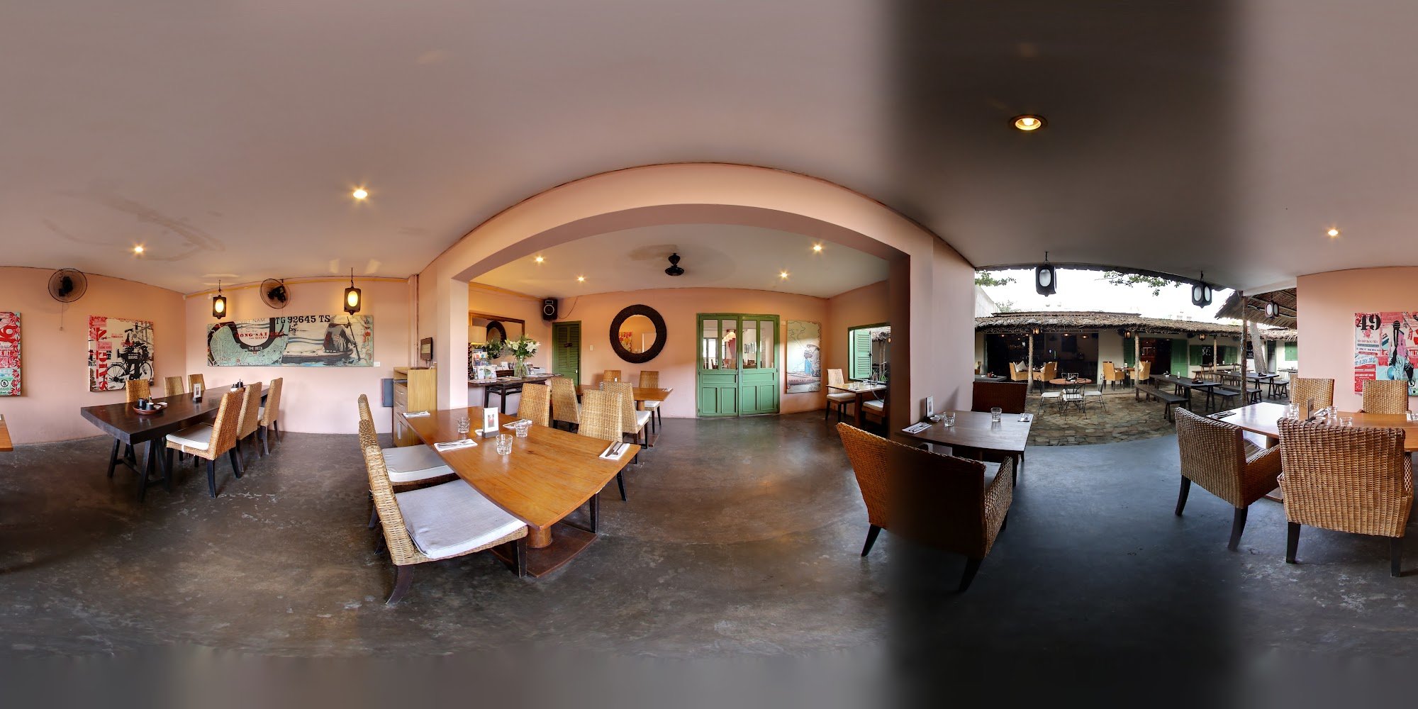 A panoramic view of a spacious restaurant interior in Thao Dien, Saigon, featuring peach-colored walls, dark concrete flooring, and a mix of indoor an