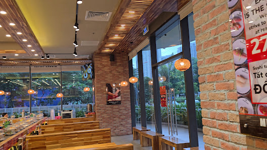 The image depicts the interior of a modern restaurant in Thao Dien, Saigon. It features wooden benches arranged in rows, exposed brick walls, large gl
