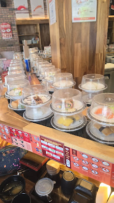 The image depicts the interior of a restaurant in Thao Dien, Saigon, focusing on a food display counter. Multiple clear plastic domes cover various fo