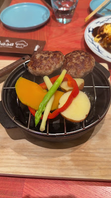 A grill pan containing two patties and a variety of vegetables including asparagus, red bell pepper slices, yellow squash, and potatoes.