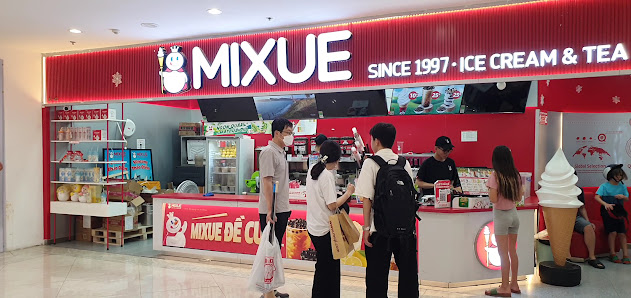 The image shows an interior view of a Mixue ice cream and tea store in Thao Dien, Saigon. The storefront is prominently displayed with red branding fe