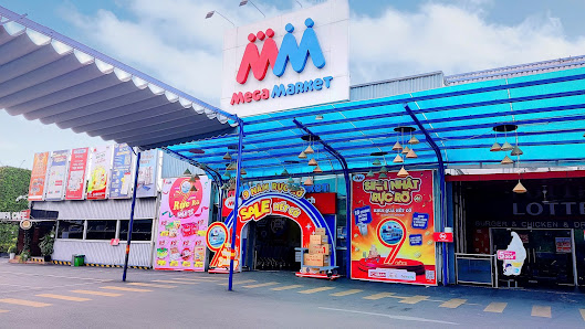 The image depicts the exterior of a Mega Market store located in Thao Dien, Saigon. The building features a blue and white canopy with the Mega Market