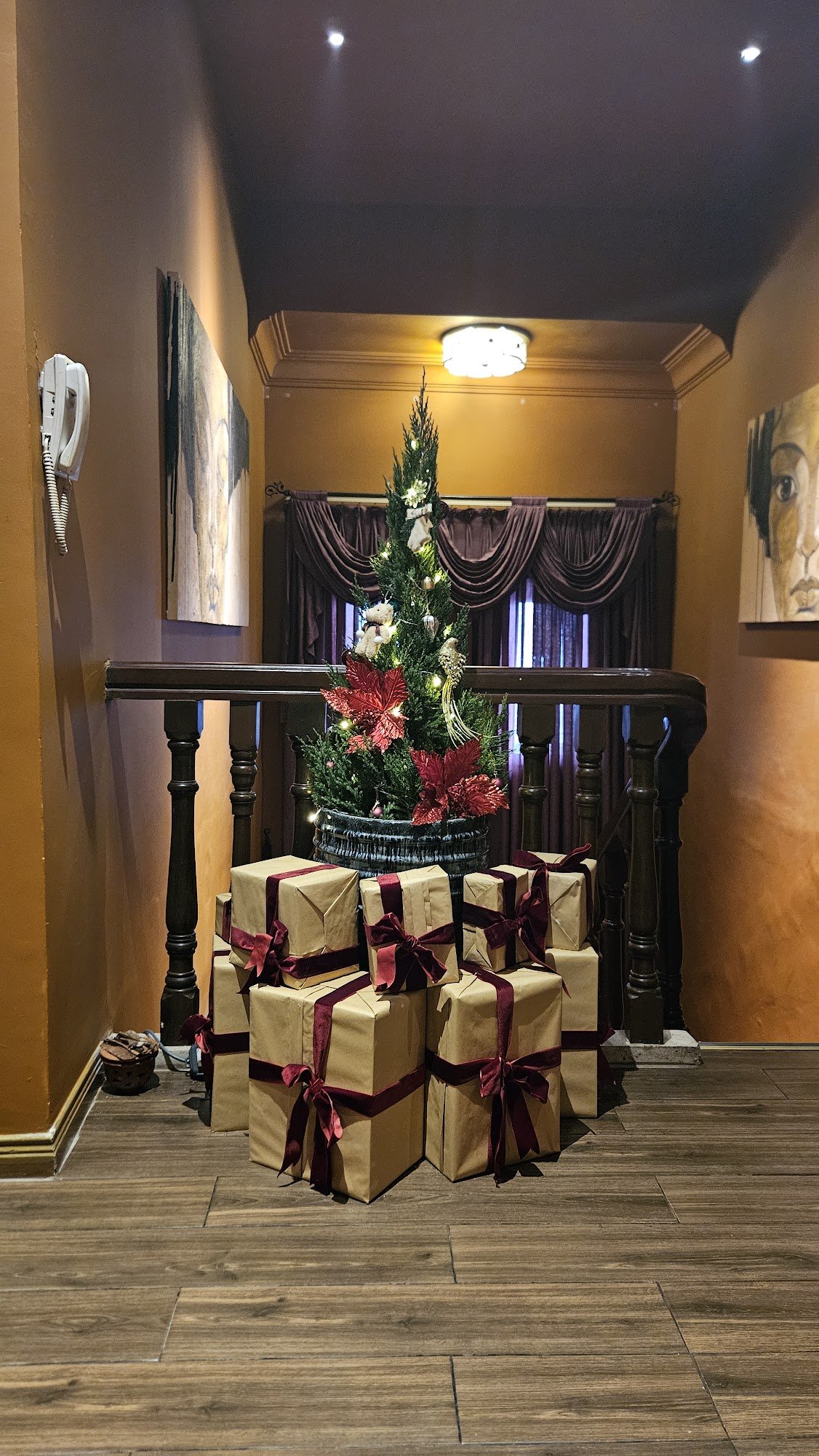 An interior hallway with a wooden staircase railing, a small Christmas tree in a basket adorned with red foliage, white ornaments, and a teddy bear, s