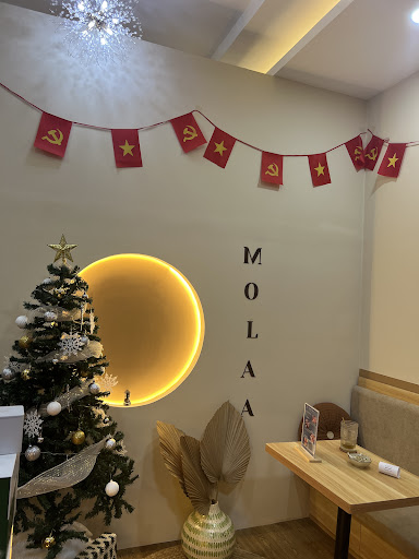 The image shows an interior space of a venue named 'MOLALA'. The decor includes festive elements such as red flags with yellow stars, a Christmas tree