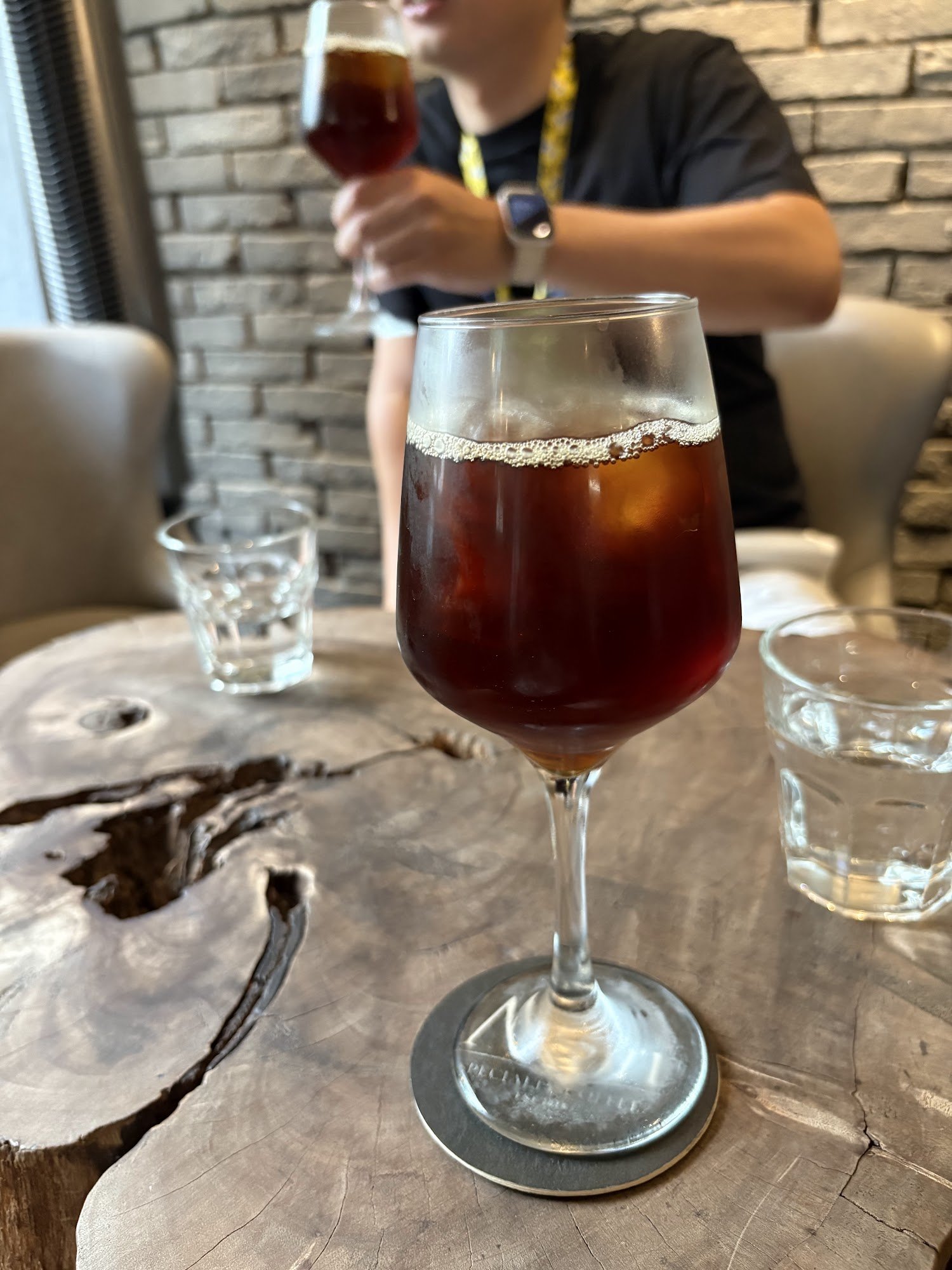 A person is seated at a table in what appears to be an indoor setting, possibly a cafe or restaurant. The focus of the image is on two glasses filled 