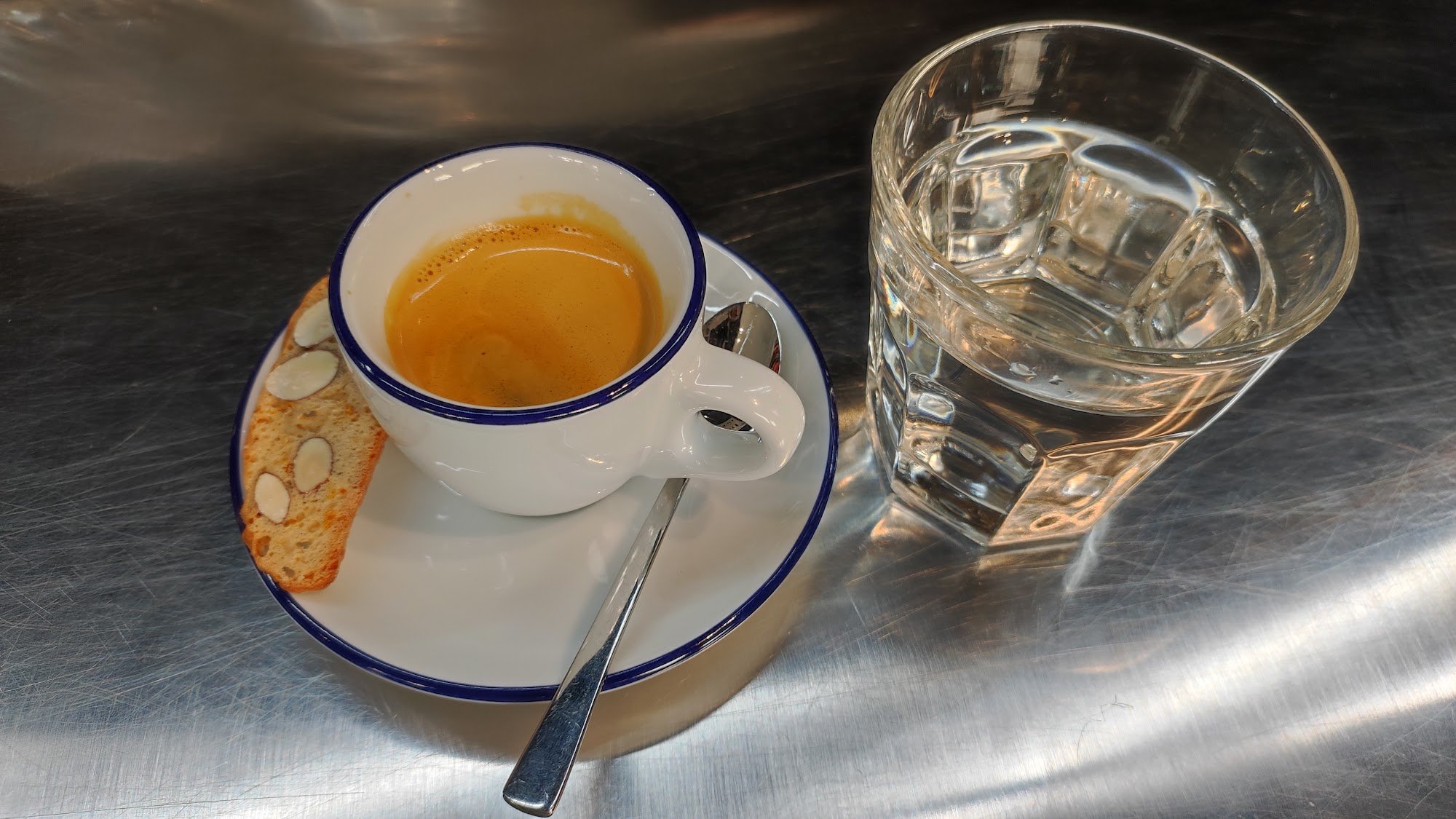 A close-up of a cup of coffee and a glass of water on a metallic table surface in what appears to be an indoor setting, possibly within Thao Dien, Sai