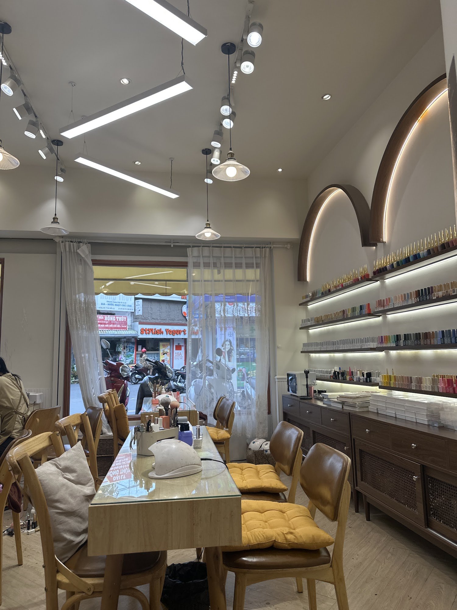 The image depicts the interior of a modern venue, likely a nail salon or beauty parlor in Thao Dien, Saigon. It features a glass-top table with chairs