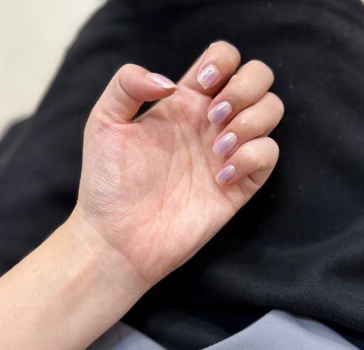 A close-up of a person's hand displaying nails painted in a gradient from light pink to clear with subtle shimmer.