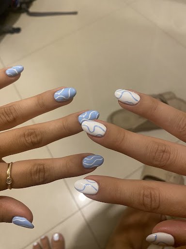Close-up of a person's hands showcasing nail art with light blue and white wavy patterns. Some nails have a light blue base with white wavy lines, whi
