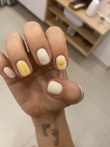 A close-up of a hand displaying manicured nails with a white base and decorative designs. The thumb and pinky have solid white polish, the index finge