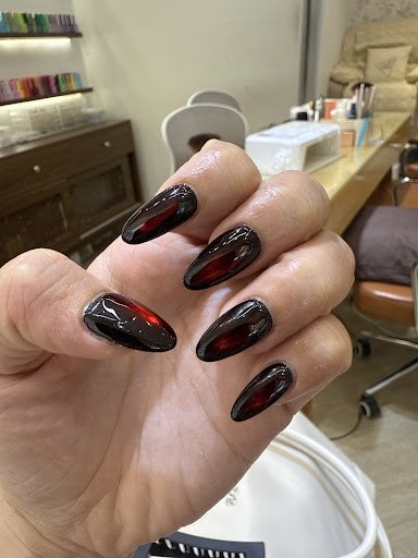 A close-up of a person's hand displaying nails painted in glossy black and red nail polish with an ombre effect, likely taken inside a beauty salon or