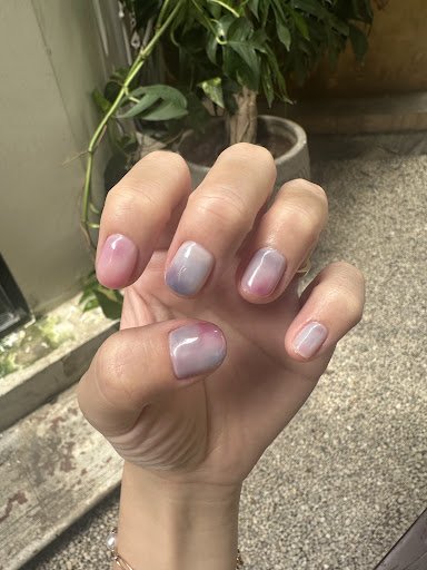 A close-up of a hand displaying nails painted in an ombre style from pink to grey gradient.