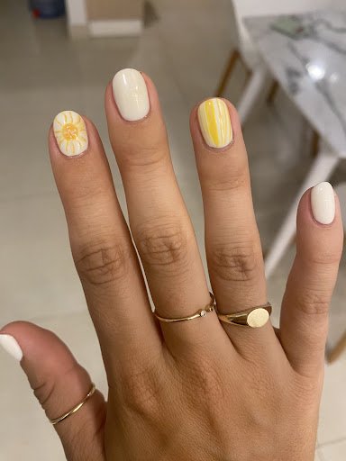 A close-up of a person's hand displaying manicured nails and rings against an indoor background with modern furnishings.