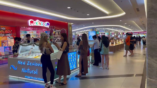 The image depicts an interior view of a shopping mall or food court area where various stalls and shops are visible. People can be seen browsing at di