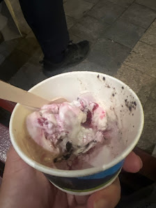 A close-up of a hand holding an ice cream cup containing what appears to be strawberry yogurt with chunks and possibly some fruit pieces, served in a