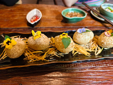 A close-up of a plated dish consisting of several spherical items garnished with flowers and served on a bed of shredded yellow strands, possibly chee