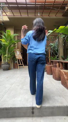A person is walking away from the camera on a paved area in what appears to be an outdoor courtyard with various plants and wooden planters.