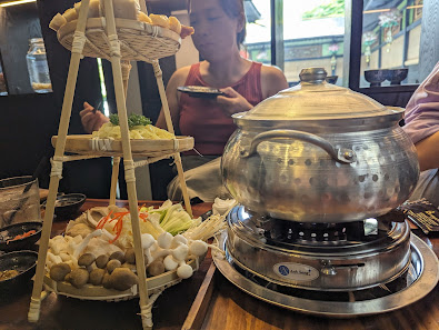 The image depicts an interior dining scene in a restaurant, likely in Thao Dien, Saigon. A large stainless steel pot sits on a gas stove, suggesting a
