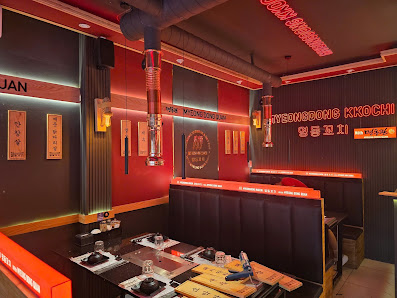 The image shows an interior view of a restaurant named 'TWINS DONG KHOCHI' with red and black decor, featuring wooden tables set for dining, neon sign