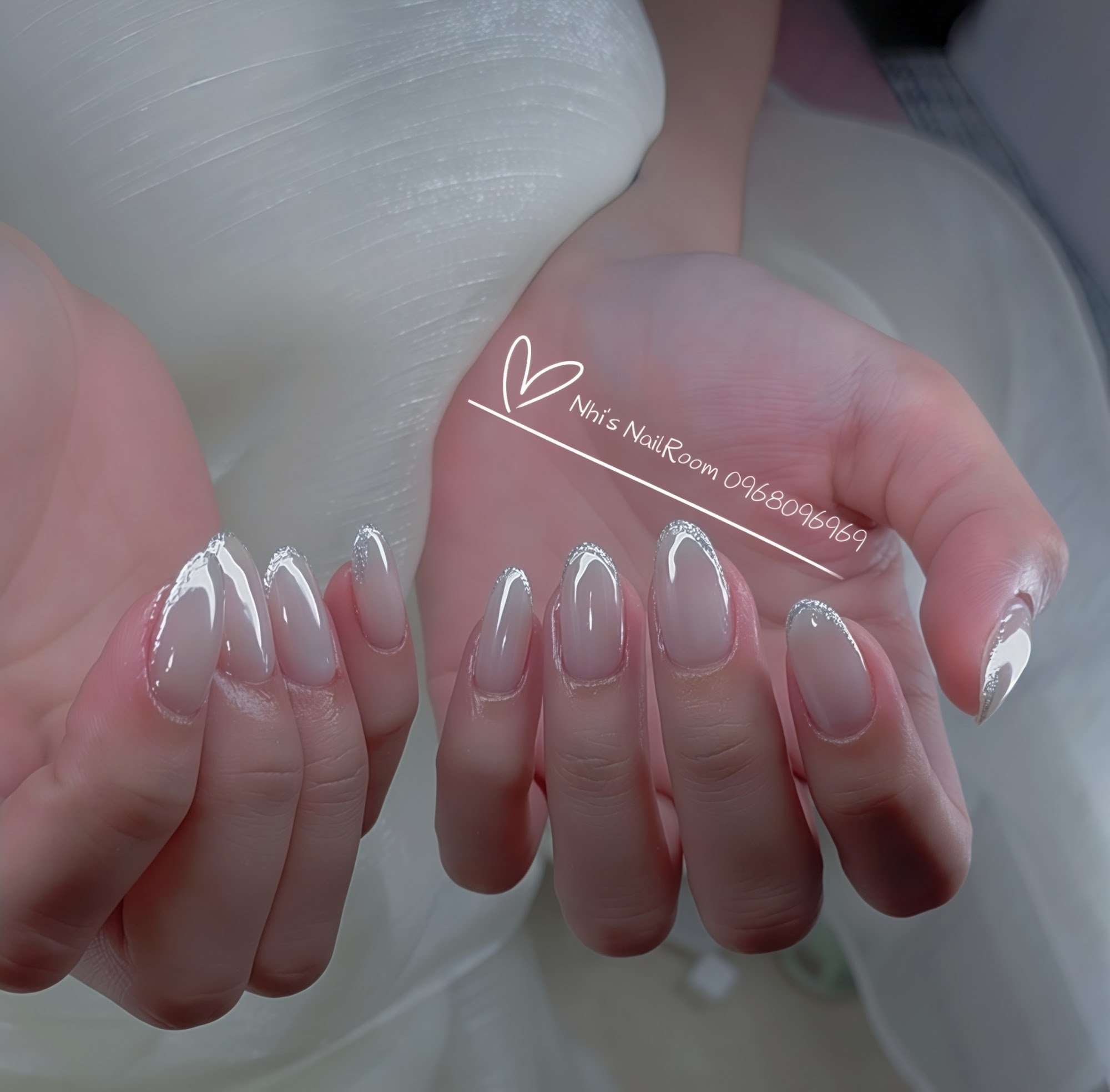 A close-up of a person's hands showcasing manicured nails with silver glitter accents on the tips and sides.