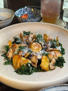 A plated dish featuring a mix of greens and what appears to be scallops or mushrooms with a creamy sauce on top, garnished with grated cheese.