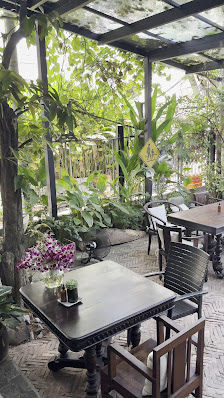 An outdoor seating area of a venue in Thao Dien, Saigon, featuring wooden tables and chairs under a covered structure with a transparent roof. Lush gr