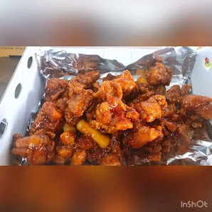 A close-up of a dish consisting of pieces of chicken coated in what appears to be a sweet and spicy sauce, served on tinfoil within a white container.